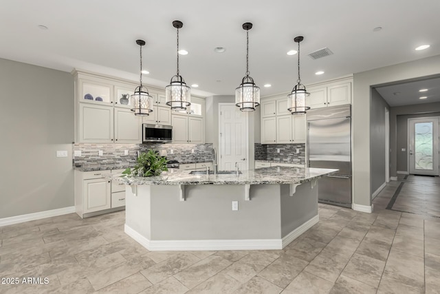 kitchen featuring pendant lighting, sink, a kitchen island with sink, light stone countertops, and stainless steel appliances