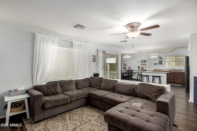 living room featuring ceiling fan with notable chandelier, dark hardwood / wood-style floors, sink, and a textured ceiling