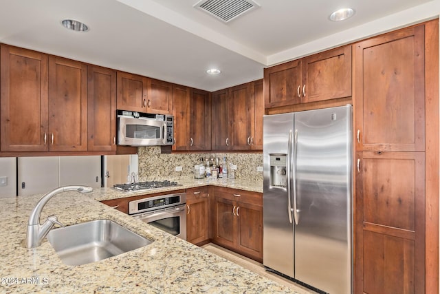 kitchen with light stone countertops, appliances with stainless steel finishes, backsplash, and sink