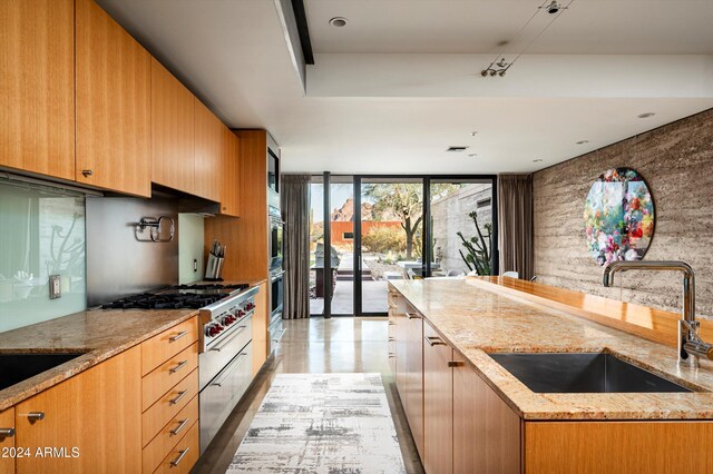 kitchen featuring floor to ceiling windows, light stone counters, sink, and appliances with stainless steel finishes