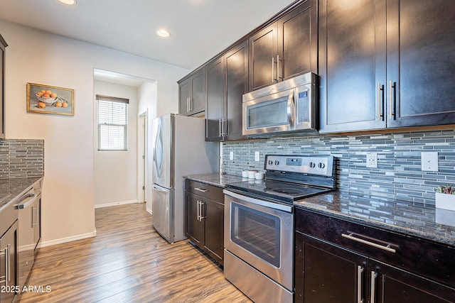 kitchen with appliances with stainless steel finishes, dark stone countertops, wood finished floors, and dark brown cabinetry