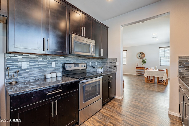 kitchen with dark stone counters, appliances with stainless steel finishes, dark wood-type flooring, and backsplash