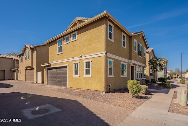 view of side of property with a garage, a tiled roof, decorative driveway, a residential view, and stucco siding