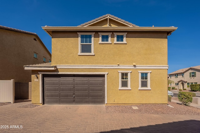 traditional-style house featuring decorative driveway, a tile roof, an attached garage, and stucco siding