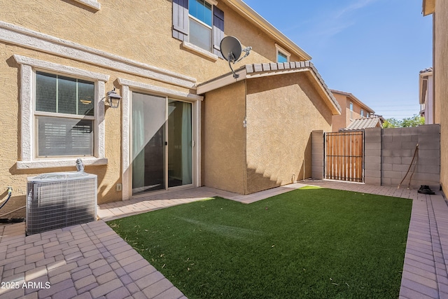 back of house with central AC unit, fence, a lawn, a gate, and stucco siding