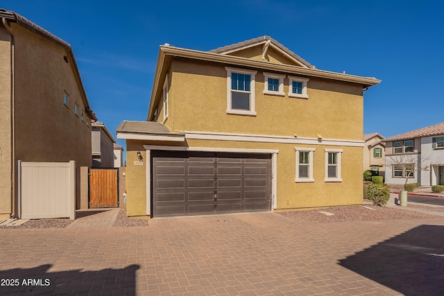 view of front of house with a garage, a tile roof, a gate, decorative driveway, and stucco siding