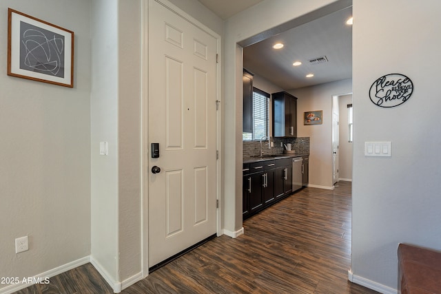 hallway with dark wood-type flooring, visible vents, a sink, and baseboards