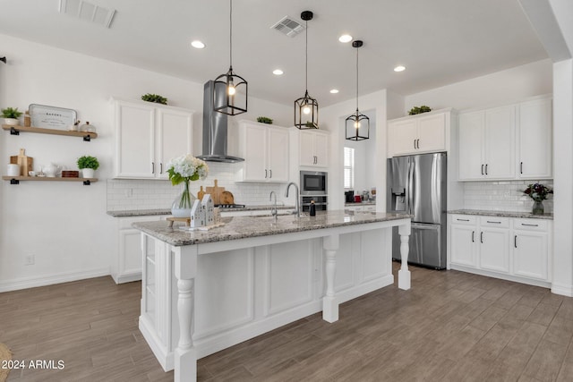 kitchen with hardwood / wood-style floors, white cabinets, wall chimney range hood, and appliances with stainless steel finishes