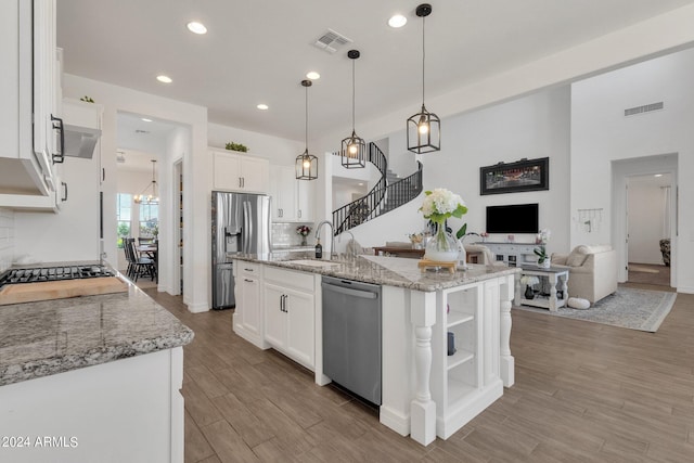 kitchen featuring decorative light fixtures, stainless steel appliances, white cabinetry, and an island with sink