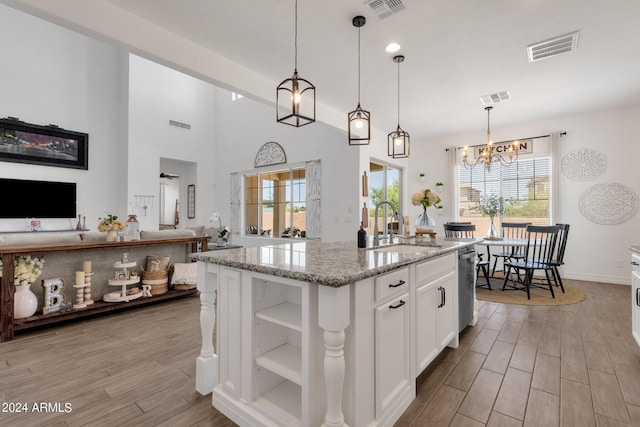 kitchen with white cabinetry, a wealth of natural light, light stone counters, and a kitchen island with sink