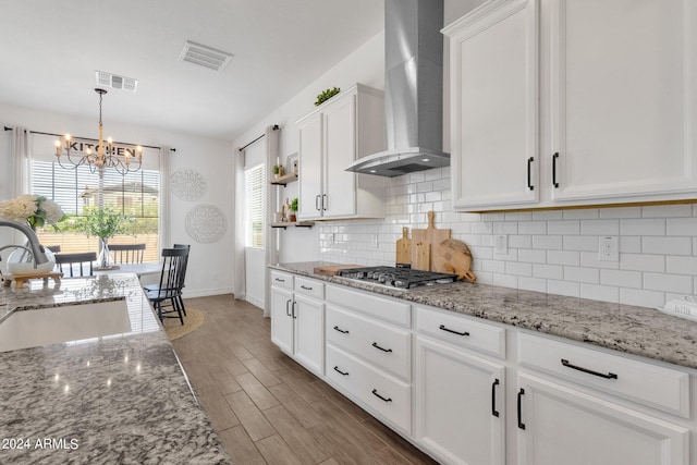 kitchen featuring wall chimney exhaust hood, stainless steel gas cooktop, sink, wood-type flooring, and white cabinetry