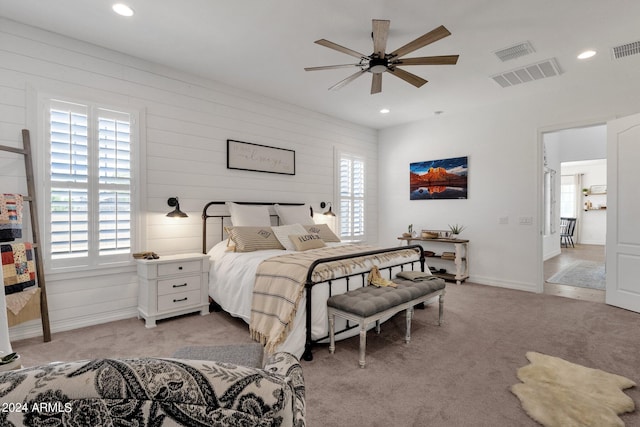 bedroom featuring ceiling fan, light colored carpet, and wood walls