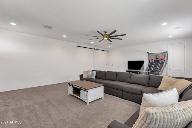 living room with ceiling fan, a barn door, and light carpet