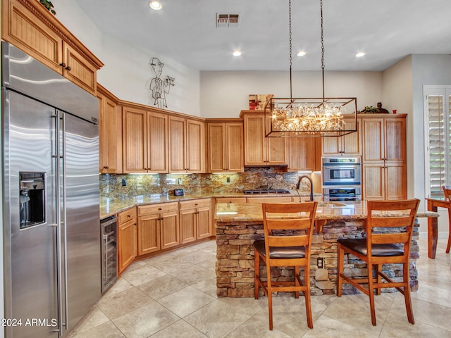 kitchen featuring a chandelier, light stone counters, beverage cooler, stainless steel appliances, and decorative light fixtures