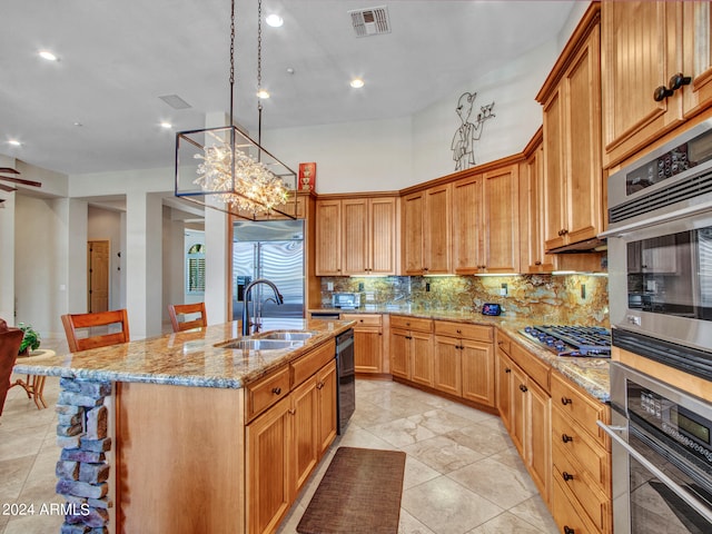 kitchen with decorative backsplash, light stone counters, a breakfast bar, a center island with sink, and sink