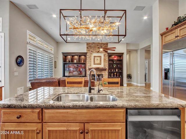 kitchen featuring light stone counters, ceiling fan with notable chandelier, pendant lighting, beverage cooler, and sink