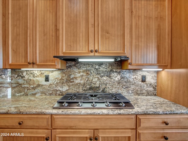 kitchen with stainless steel gas stovetop, backsplash, and light stone countertops