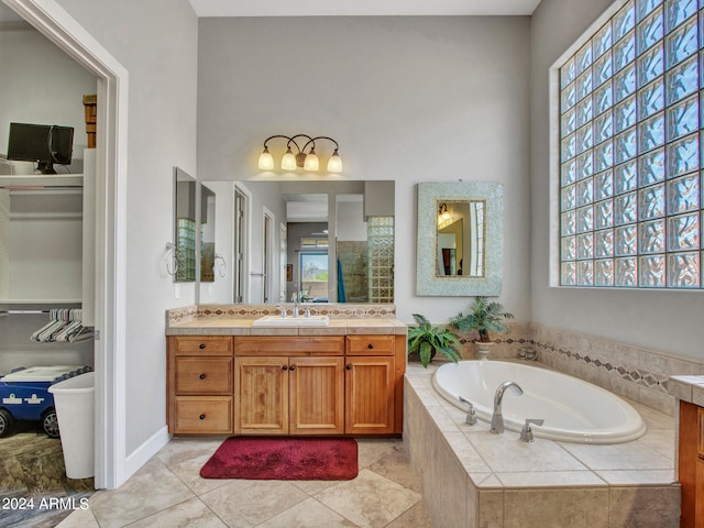 bathroom featuring a healthy amount of sunlight, tile patterned floors, tiled tub, and vanity