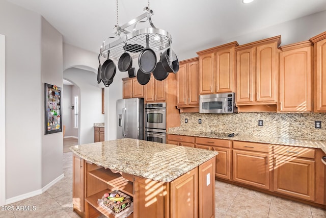 kitchen with light tile patterned floors, tasteful backsplash, light stone counters, a kitchen island, and appliances with stainless steel finishes