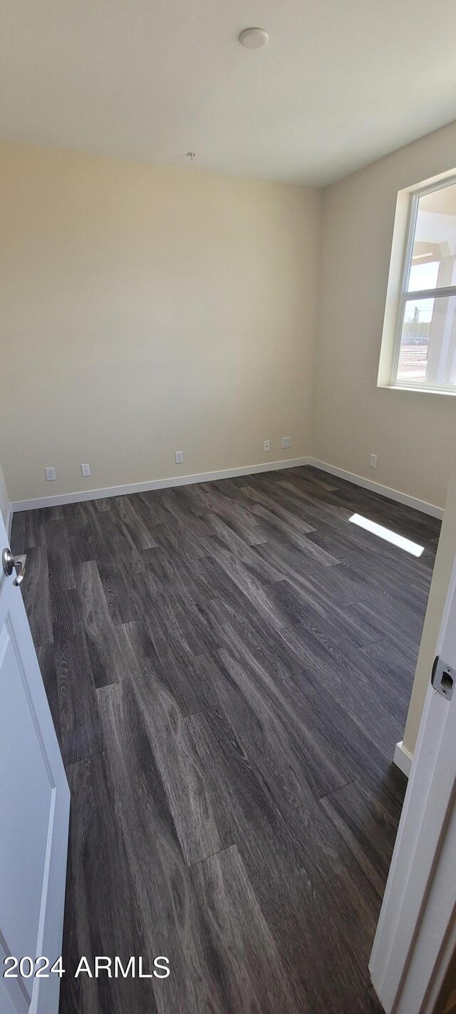 spare room with baseboards and dark wood-type flooring