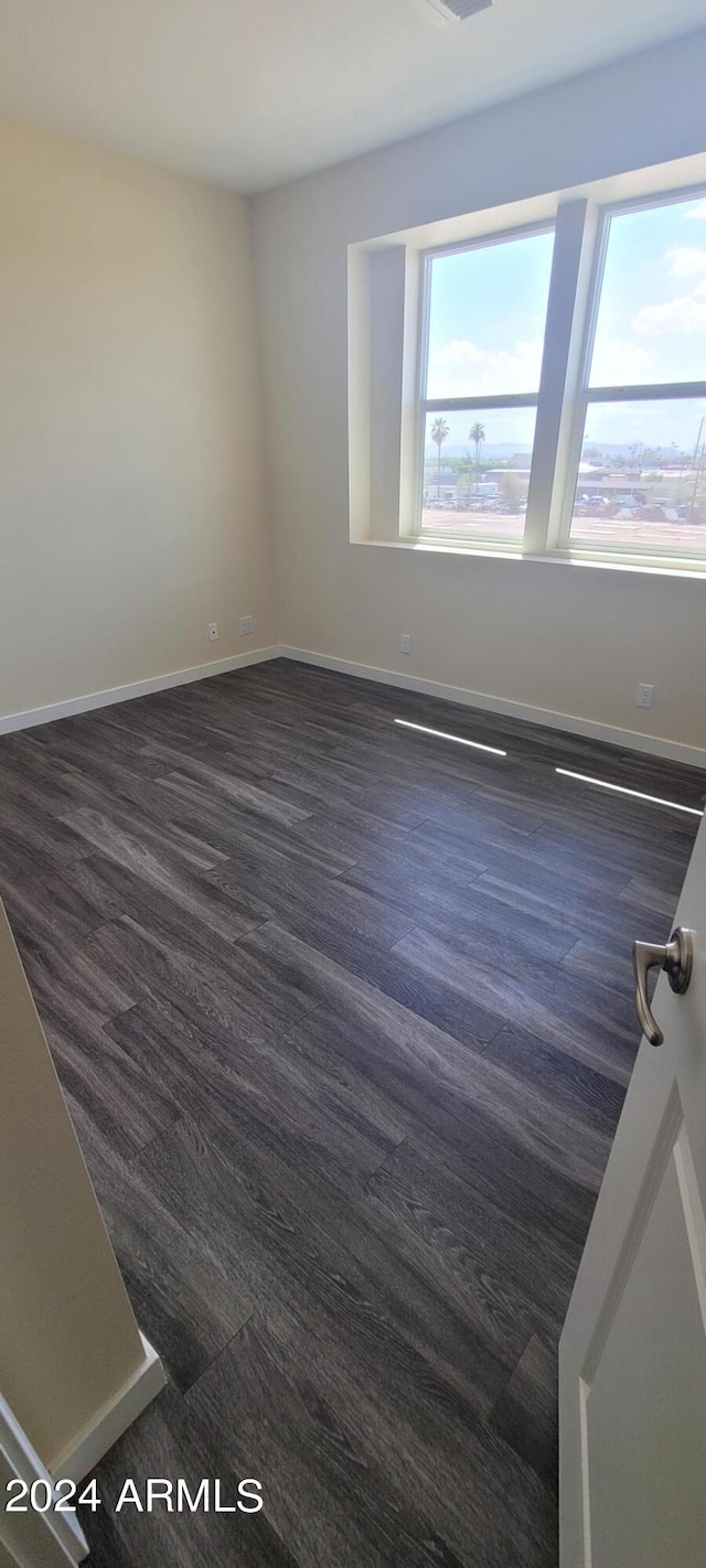 empty room featuring baseboards, dark wood finished floors, and a wealth of natural light