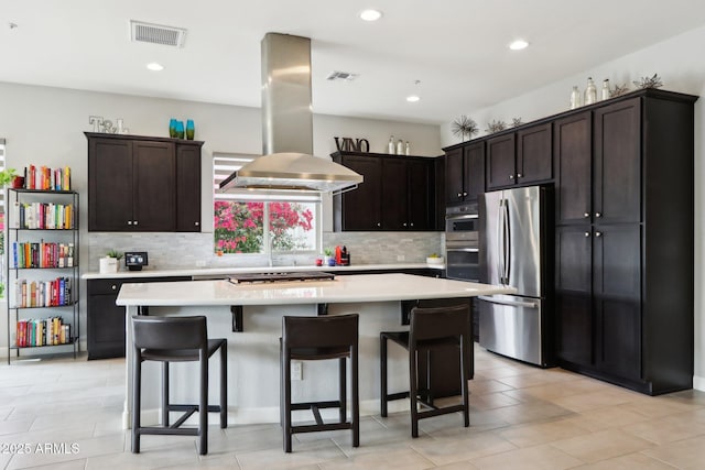 kitchen with island exhaust hood, appliances with stainless steel finishes, a center island, and backsplash