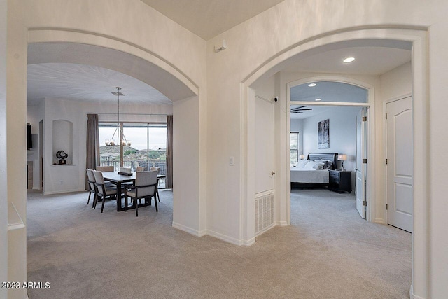 hallway with light colored carpet and an inviting chandelier