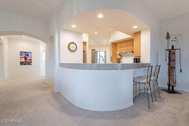 kitchen featuring a kitchen bar, light brown cabinetry, light colored carpet, and sink