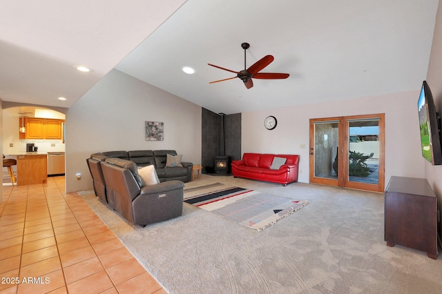 living room featuring a wood stove, ceiling fan, light tile patterned floors, and vaulted ceiling