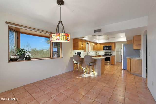 kitchen featuring sink, a tray ceiling, a kitchen bar, kitchen peninsula, and stainless steel appliances