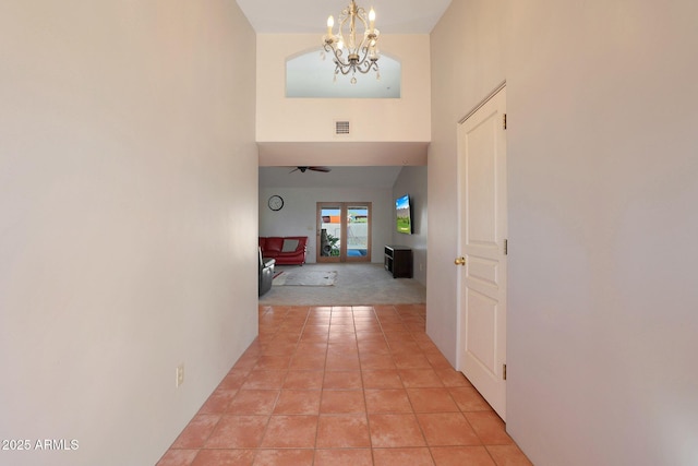 hallway with a high ceiling, a notable chandelier, and light tile patterned flooring