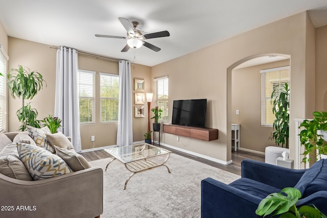 living room featuring a ceiling fan, baseboards, arched walkways, and wood finished floors