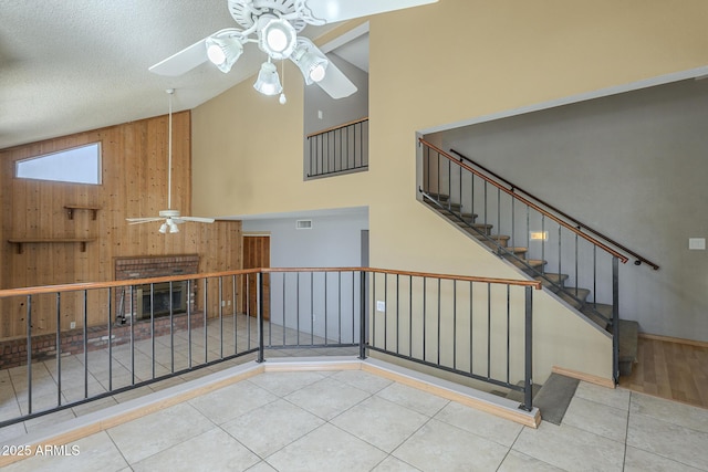 interior space featuring stairway, a ceiling fan, wood walls, a textured ceiling, and high vaulted ceiling