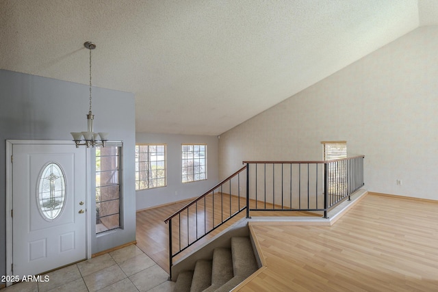 foyer with stairway, a chandelier, vaulted ceiling, and wood finished floors