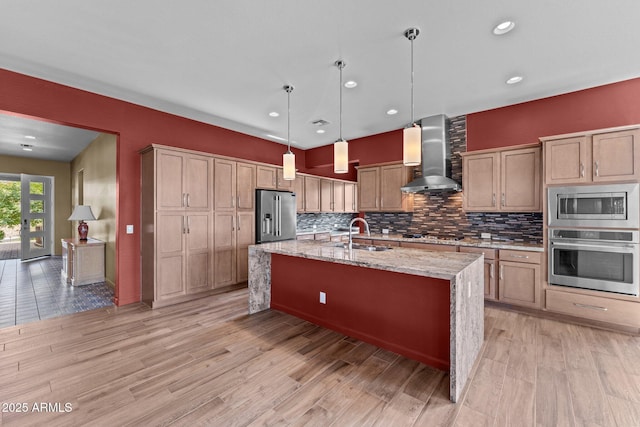 kitchen featuring light wood-style flooring, a sink, decorative backsplash, wall chimney exhaust hood, and stainless steel appliances