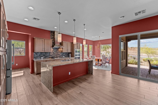 kitchen featuring light stone counters, appliances with stainless steel finishes, visible vents, and wall chimney exhaust hood