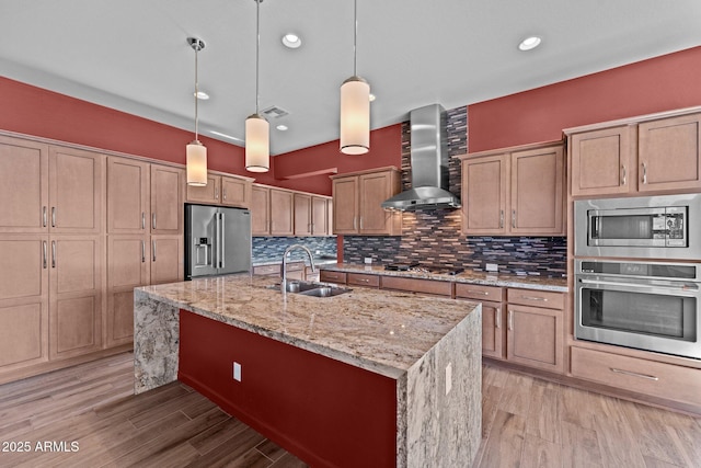 kitchen with light wood-style flooring, a sink, stainless steel appliances, wall chimney range hood, and decorative backsplash