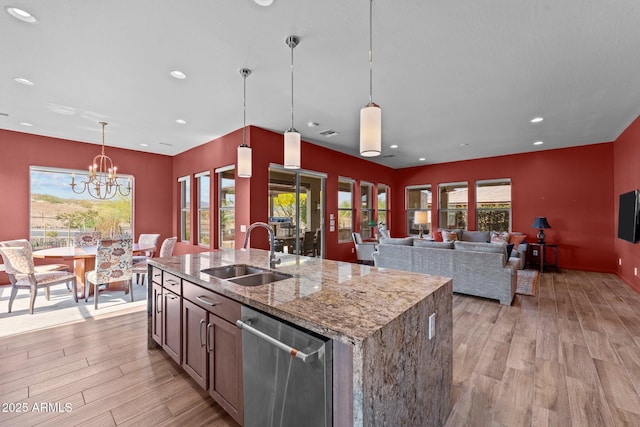 kitchen with dishwasher, light stone counters, a sink, light wood-style floors, and an island with sink