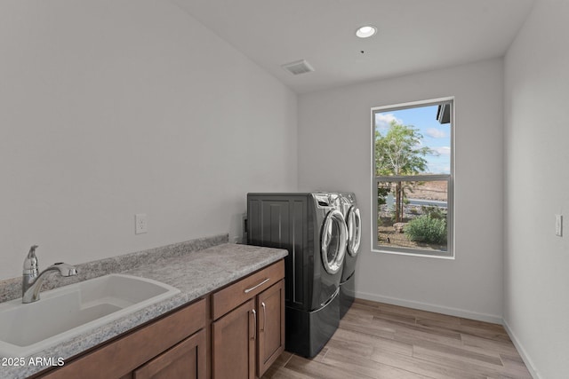 clothes washing area featuring a sink, cabinet space, separate washer and dryer, visible vents, and light wood-style floors