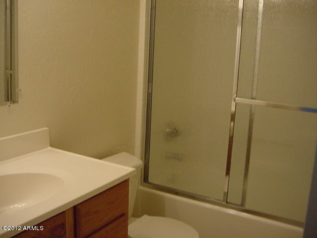 full bath featuring toilet, enclosed tub / shower combo, and vanity