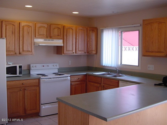 kitchen featuring a peninsula, white appliances, under cabinet range hood, a sink, and light tile patterned floors