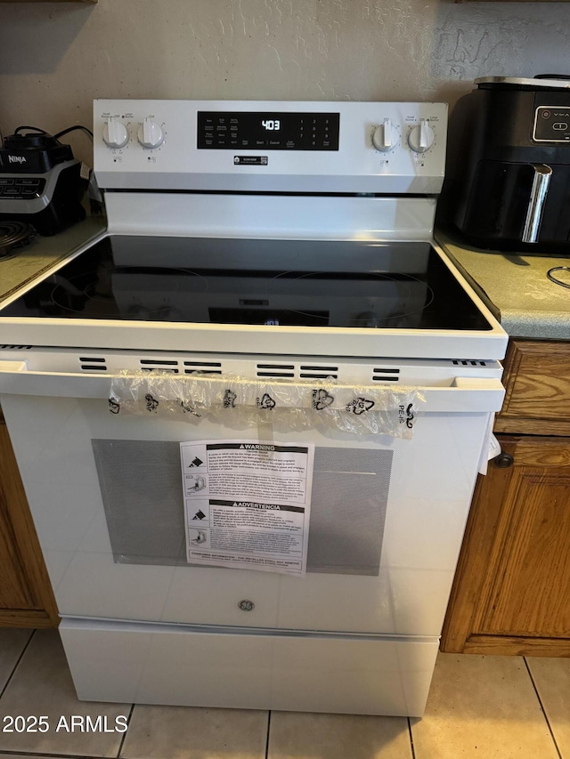 interior details featuring light countertops, white range with electric stovetop, and brown cabinets