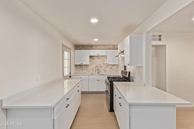 kitchen featuring a sink, double oven range, under cabinet range hood, backsplash, and light countertops