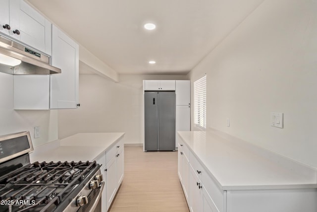 kitchen with under cabinet range hood, light countertops, light wood-style floors, white cabinets, and stainless steel appliances