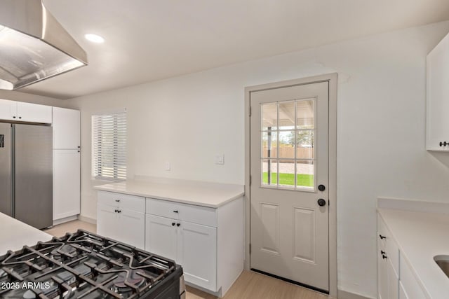 kitchen with black gas range oven, white cabinets, stainless steel refrigerator, and light countertops