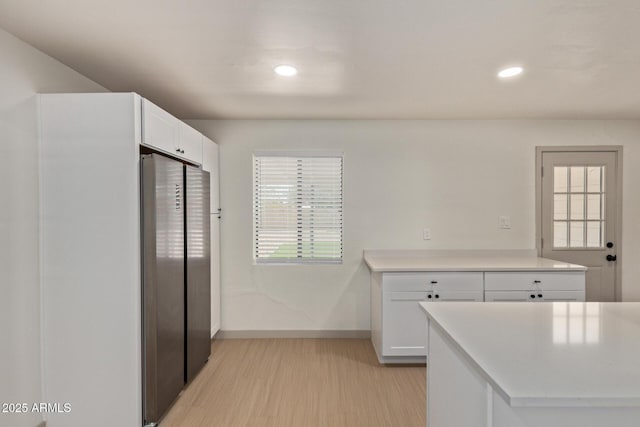 kitchen with baseboards, light wood finished floors, freestanding refrigerator, light countertops, and white cabinetry