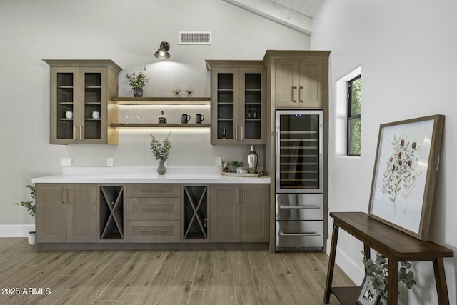 bar with beverage cooler, light wood-style floors, vaulted ceiling, and visible vents