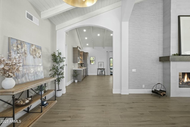 entrance foyer with a tile fireplace, arched walkways, high vaulted ceiling, and visible vents