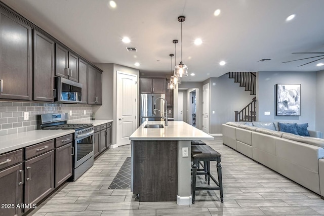 kitchen featuring a breakfast bar, pendant lighting, backsplash, stainless steel appliances, and a center island with sink