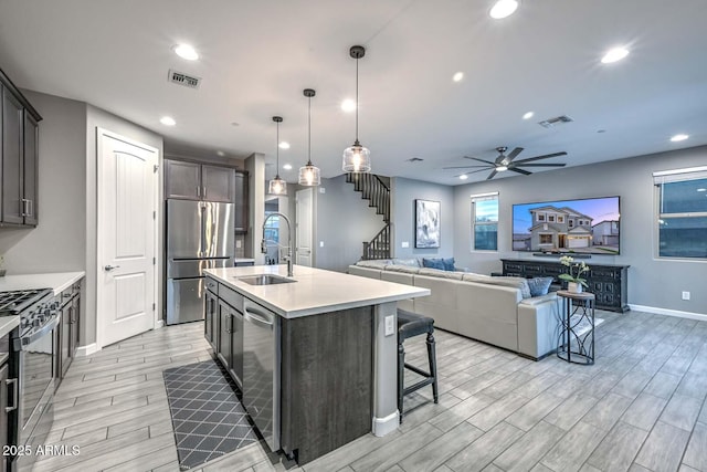 kitchen featuring pendant lighting, sink, a center island with sink, stainless steel appliances, and a kitchen bar